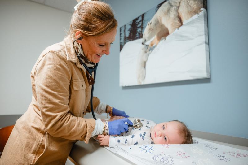 a female pediatrician looking at a baby on an exam table